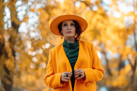 Beautiful woman walks outdoors in autumn. She is wearing a yellow coat, yellow hat and green dress. Young woman enjoying the autumn weather. Autumn content.