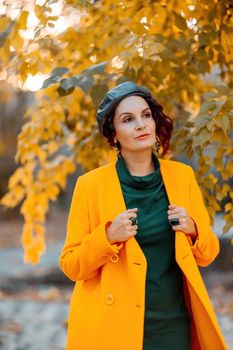 Beautiful woman walks outdoors in autumn. She is wearing a yellow coat and a green dress. Young woman enjoying the autumn weather. Autumn content