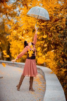 Beautiful girl in a dress with an umbrella in the autumn park. She holds him over her head, autumn leaves are falling out of him.