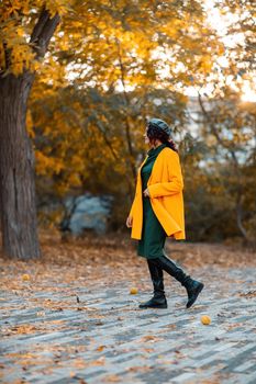 Beautiful woman walks outdoors in autumn. She is wearing a yellow coat and a green dress. Young woman enjoying the autumn weather. Autumn content