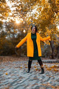 Beautiful woman walks outdoors in autumn. She is wearing a yellow coat and a green dress. Young woman enjoying the autumn weather. Autumn content