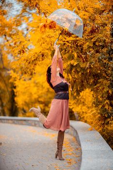 Beautiful girl in a dress with an umbrella in the autumn park. She holds him over her head, autumn leaves are falling out of him.