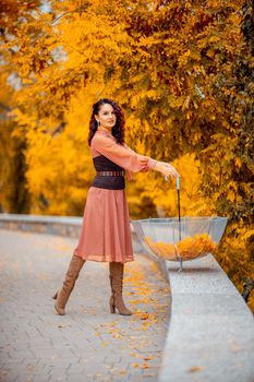 Beautiful girl in a dress with an umbrella in the autumn park. She holds him over her head, autumn leaves are falling out of him.