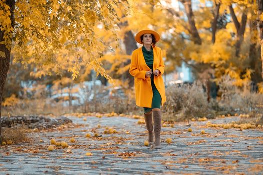 Beautiful woman walks outdoors in autumn. She is wearing a yellow coat, yellow hat and green dress. Young woman enjoying the autumn weather. Autumn content.