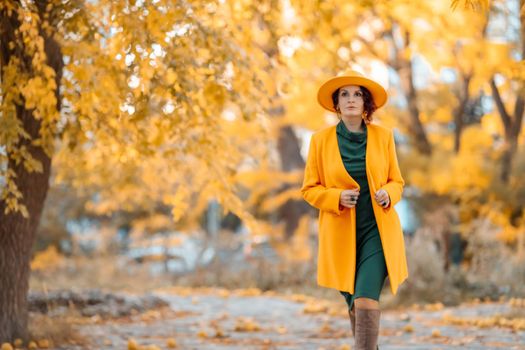 Beautiful woman walks outdoors in autumn. She is wearing a yellow coat, yellow hat and green dress. Young woman enjoying the autumn weather. Autumn content.