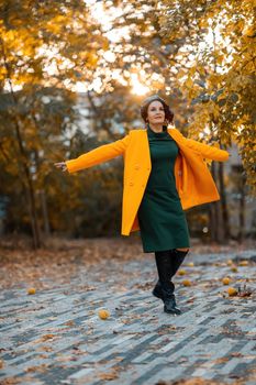 Beautiful woman walks outdoors in autumn. She is wearing a yellow coat and a green dress. Young woman enjoying the autumn weather. Autumn content