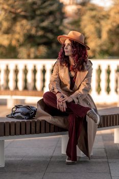 Outdoor fashion portrait of young elegant fashionable brunette woman, model in stylish hat, choker and light raincoat posing at sunset in European city