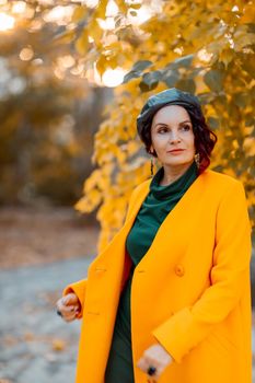 Beautiful woman walks outdoors in autumn. She is wearing a yellow coat and a green dress. Young woman enjoying the autumn weather. Autumn content