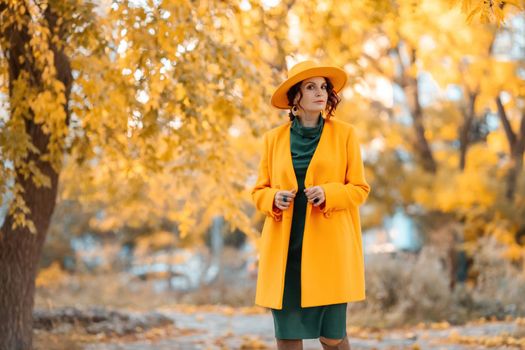 Beautiful woman walks outdoors in autumn. She is wearing a yellow coat, yellow hat and green dress. Young woman enjoying the autumn weather. Autumn content.