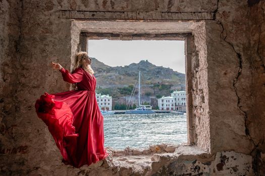 View of Balaklava Bay through an arched balcony in oriental style. The girl in a long red dress stands with her back. Abandoned mansion on the Black Sea coast.