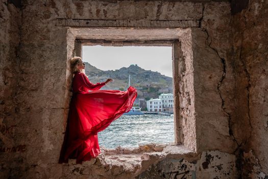 View of Balaklava Bay through an arched balcony in oriental style. The girl in a long red dress stands with her back. Abandoned mansion on the Black Sea coast.