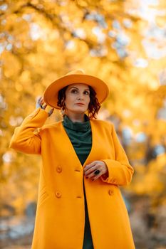 Beautiful woman walks outdoors in autumn. She is wearing a yellow coat, yellow hat and green dress. Young woman enjoying the autumn weather. Autumn content.