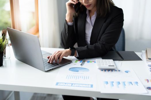 Business correspondence, consultation, portrait of an Asian woman on the phone talking and planning financial statements and investments and using computers and documents to analyze financial systems