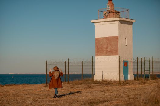 A woman walking along the coast near the sea. An elegant lady in a brown coat and a hat with fashionable makeup walks on the seashore.