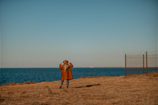 A woman walking along the coast near the sea. An elegant lady in a brown coat and a hat with fashionable makeup walks on the seashore.