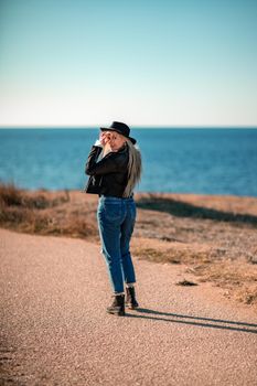 A blonde in a stylish black leather jacket walks along the seashore