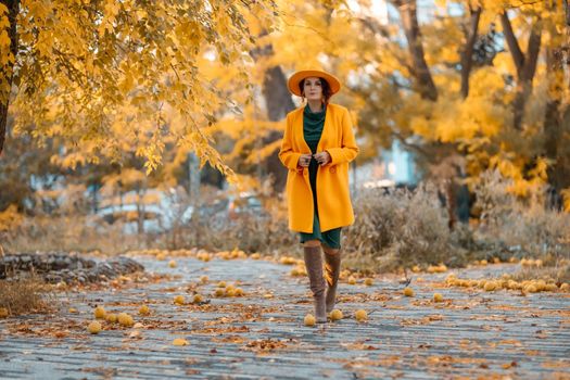 Beautiful woman walks outdoors in autumn. She is wearing a yellow coat, yellow hat and green dress. Young woman enjoying the autumn weather. Autumn content.