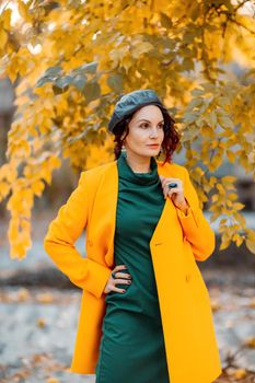 Beautiful woman walks outdoors in autumn. She is wearing a yellow coat and a green dress. Young woman enjoying the autumn weather. Autumn content