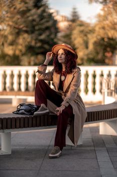 Outdoor fashion portrait of young elegant fashionable brunette woman, model in stylish hat, choker and light raincoat posing at sunset in European city