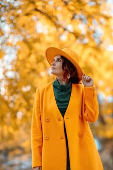 Beautiful woman walks outdoors in autumn. She is wearing a yellow coat, yellow hat and green dress. Young woman enjoying the autumn weather. Autumn content.