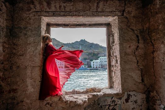 View of Balaklava Bay through an arched balcony in oriental style. The girl in a long red dress stands with her back. Abandoned mansion on the Black Sea coast.