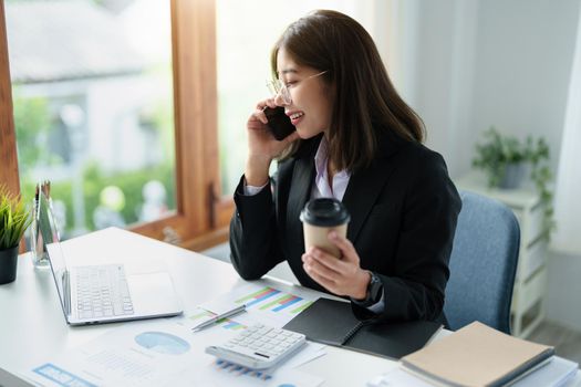 Business correspondence, consultation, portrait of an Asian woman on the phone talking and planning financial statements and investments and using computers and documents to analyze financial systems