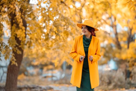 Beautiful woman walks outdoors in autumn. She is wearing a yellow coat, yellow hat and green dress. Young woman enjoying the autumn weather. Autumn content.