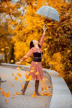 Beautiful girl in a dress with an umbrella in the autumn park. She holds him over her head, autumn leaves are falling out of him.