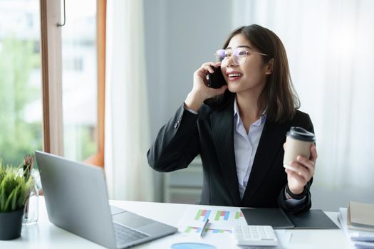 Business correspondence, consultation, portrait of an Asian woman on the phone talking and planning financial statements and investments and using computers and documents to analyze financial systems