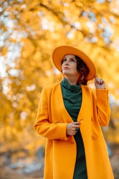 Beautiful woman walks outdoors in autumn. She is wearing a yellow coat, yellow hat and green dress. Young woman enjoying the autumn weather. Autumn content.