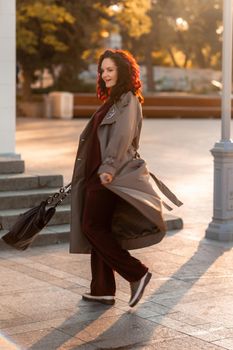 Outdoor fashion portrait of young elegant fashionable brunette woman, model in stylish hat, choker and light raincoat posing at sunset in European city