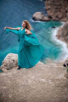 A woman in an emerald dress, a fashion model with long silk wings in a flowing dress, flying fabric on the embankment