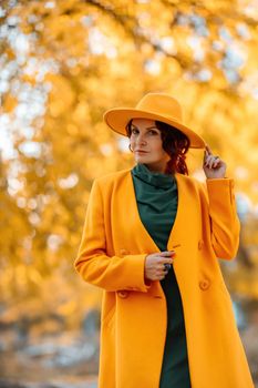 Beautiful woman walks outdoors in autumn. She is wearing a yellow coat, yellow hat and green dress. Young woman enjoying the autumn weather. Autumn content.