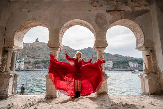 View of Balaklava Bay through an arched balcony in oriental style. The girl in a long red dress stands with her back. Abandoned mansion on the Black Sea coast.