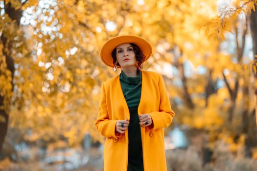 Beautiful woman walks outdoors in autumn. She is wearing a yellow coat, yellow hat and green dress. Young woman enjoying the autumn weather. Autumn content.