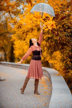 Beautiful girl in a dress with an umbrella in the autumn park. She holds him over her head, autumn leaves are falling out of him.