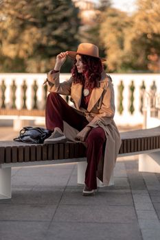 Outdoor fashion portrait of young elegant fashionable brunette woman, model in stylish hat, choker and light raincoat posing at sunset in European city