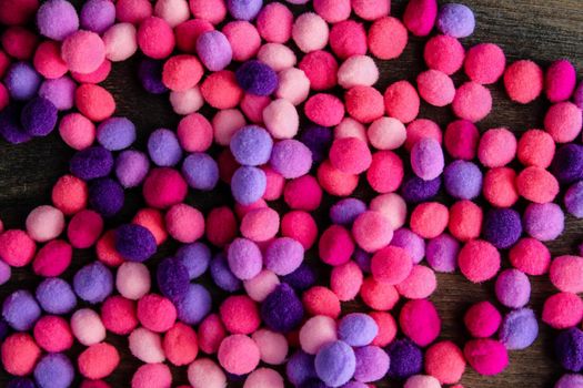 Round pink and purple fluffy balls pompoms on wooden background. Bunch of poppoms