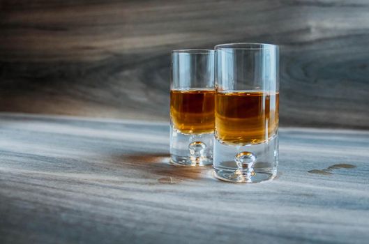 Two shot glasses with whiskey on a wooden background