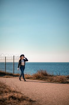 A blonde in a stylish black leather jacket walks along the seashore