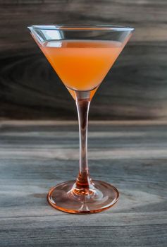 Martini glass of orange cocktail on a wooden table