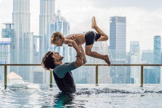 Father and son in outdoor swimming pool with city view in blue sky.