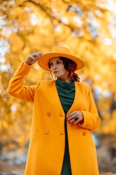 Beautiful woman walks outdoors in autumn. She is wearing a yellow coat, yellow hat and green dress. Young woman enjoying the autumn weather. Autumn content.