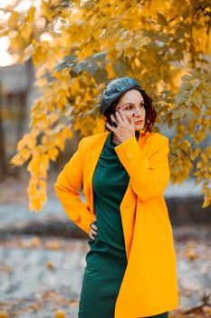 Beautiful woman walks outdoors in autumn. She is wearing a yellow coat and a green dress. Young woman enjoying the autumn weather. Autumn content