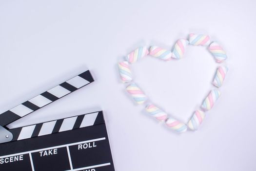 Movie clapperboard with heart shaped from twisted marshmallows. Valentine's day concept. Love. White background with twisted marshmallow pattern. Mock up. Space for text.