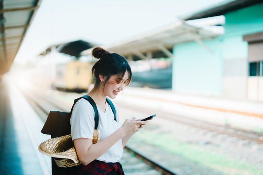 summer, relax, vacation, travel, portrait of beautiful Asian girl using the smartphone mobile to call friends at the train station while waiting for their travel time