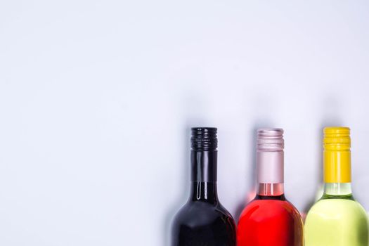 Red, rose and white wine bottles on white table. Top view with copy space