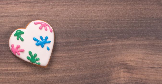 Colorful heart shaped glazed cookie for Valentine's day on wooden background. Paint splatter. Space for text. Easter cookie.