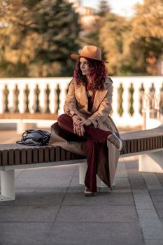 Outdoor fashion portrait of young elegant fashionable brunette woman, model in stylish hat, choker and light raincoat posing at sunset in European city