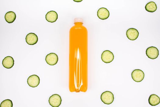 Bottle of orange smoothie on white background cucumber pattern. Top view. Detox summer drink. Healthy fresh juice bottle. Vegan and vegetarian concept.